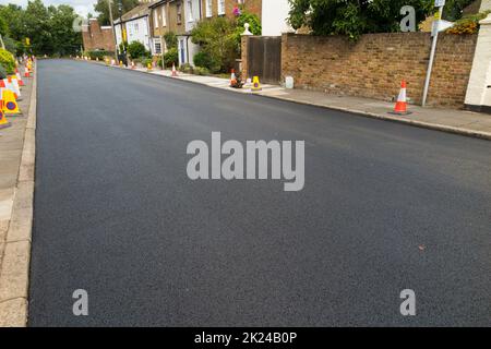 Eine schöne frisch neu verlegte Schicht aus heißem, frischem und glattem Asphalt auf der Straße, kurz nachdem eine Walzenglättung und Walzmaschine den Tarmakadam gerollt hat. Die neue Oberfläche wurde bei der Sanierung einer Wohnstraße in Twickenham, Großraum London, Großbritannien, verlegt. (132) Stockfoto