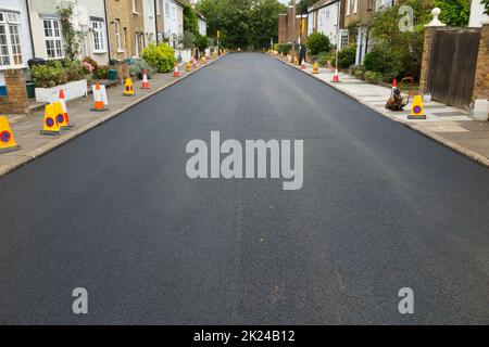 Eine schöne frisch neu verlegte Schicht aus heißem, frischem und glattem Asphalt auf der Straße, kurz nachdem eine Walzenglättung und Walzmaschine den Tarmakadam gerollt hat. Die neue Oberfläche wurde bei der Sanierung einer Wohnstraße in Twickenham, Großraum London, Großbritannien, verlegt. (132) Stockfoto
