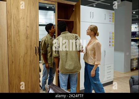 Multi-ethnische Familie Paar Käufer Suche Kleiderschrank für neue Hauswohnung. Einkaufen im Möbelgeschäft Stockfoto