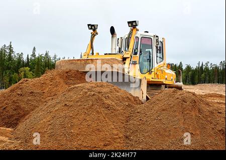 Ein gelber Traktor legt den Standort mit Sand ab. Hochwertige Fotos Stockfoto