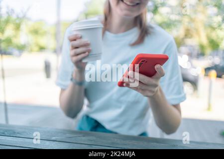 Fokussierte Nahaufnahme einer kaukasischen jungen Frau, die mit einem Smartphone-Handy für E-Banking-Fernarbeiten während des Kaffeetrinkens im Café hält Stockfoto