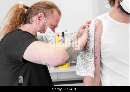 Ein erfahrener Tattoo-Künstler, der eine Skizze auf den Arm eines Mannes legt. Hochwertige Fotos Stockfoto