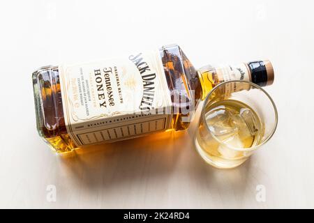 Moskau, Russland - 26. März 2022: Glas- und Liegeflasche von Jack Daniel's Tennessee Honey Likör auf hellem Tisch. Es ist Honiglikör mit weniger gemischt Stockfoto