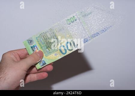 Eine in einer Hand gehaltene Euro-Banknote zerfällt und löst sich auf grauem Hintergrund auf Stockfoto