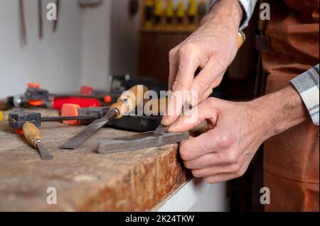 Der Zimmermann schärft den Meißel. Der Holzbearbeitungsvorgang mit den Handwerkzeugen in der Schreinerei. Das Konzept der Holzschnitzerei. Hochwertige Fotografie. Stockfoto