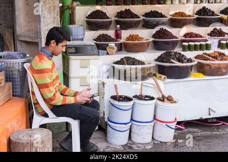 Masuleh, IRAN - 22. Dezember 2017 Teenager Verkäuferassistent Blick auf sein Handy in Gurken-Shop Stockfoto