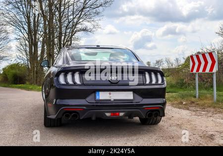 Kiel, Deutschland - 30.April 2022: Rückansicht eines schwarzen Sportwagens Ford Mustang Modell 2018, der auf einer Sandstraße geparkt ist Stockfoto