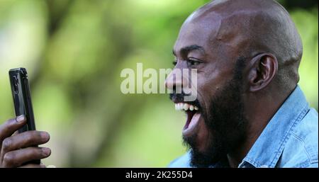 Mann begeistert von guten Nachrichten auf dem Handy, mittleren Alters afrikanische Ethnie Stockfoto