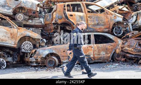 Polizeibeamte vor verbrannten Autos, die durch Raketenexplosionen zerstört wurden. Krieg in der Ukraine. Zerstörte Fahrzeuge von Zivilisten. Autofriedhof. Ukraine, Irpen Stockfoto