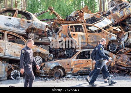 Polizeibeamte vor verbrannten Autos, die durch Raketenexplosionen zerstört wurden. Krieg in der Ukraine. Zerstörte Fahrzeuge von Zivilisten. Autofriedhof. Ukraine, Irpen Stockfoto