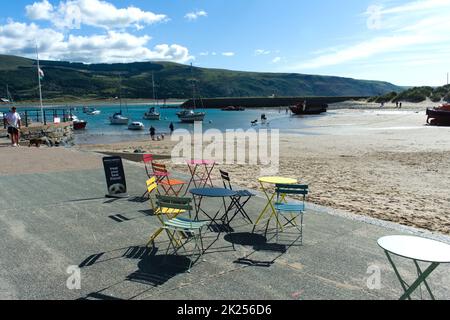 Barmouth Beach, Cardigan Bay - Wales - September 16 2022: Seascape mit farbenfrohen Café-Tischen und -Stühlen im Vordergrund. Britischer Sommer am Meer Stockfoto