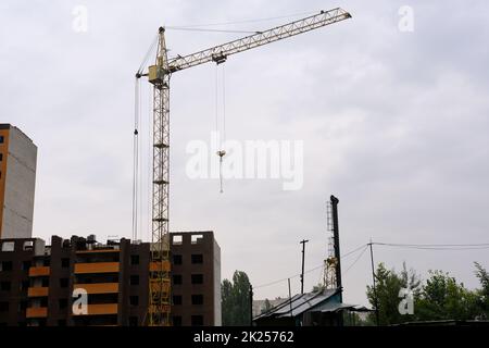 Ein Kran baut ein Haus in einer Höhe, hebt die Last in das Obergeschoss. Die Baustelle eines Wohngebäudes, ein Gebäude gegen den Himmel Stockfoto