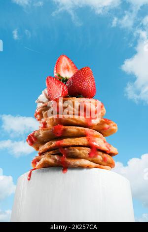 Stapel von Pfannkuchen oder Turm von Pfannkuchen von unten geschossen, perspektivischer Effekt. Kreativer Stapel von Pfannkuchen mit Beeren, Erdbeeren und appetitischem Dripp Stockfoto