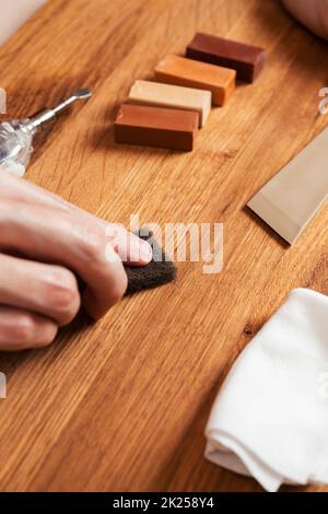 Mann füllt Risse, Kratzer, Dellen durch Wachs im Holzboden, Möbel. Professionelles Reparaturset Laminat oder Parkett mit harten Wachsstäben. Renovati Stockfoto