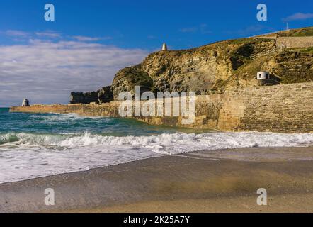 Die Wellen brechen am Pier entlang und am Strand in Portreath, einem kleinen Küstendorf in Cornwall. Auf dem Pier und den Klippen befinden sich die Aussichtstürme des Piloten. Stockfoto