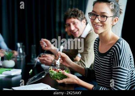 Genießen Sie das Mittagessen mit Kollegen und Freunden. Porträt eines jungen Büromitarbeiters, der mit Kollegen an einem Sitzungstisch zu Mittag isst. Stockfoto