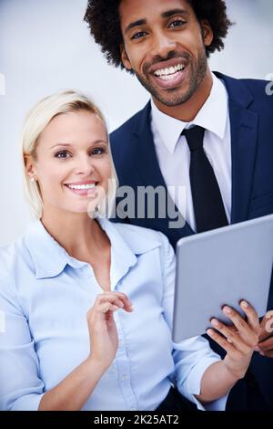Wir haben Technologie für unser Unternehmen eingesetzt. Portait hat zwei Kollegen fotografiert, die fröhlich zusammen lächeln und dabei ein digitales Tablet halten. Stockfoto