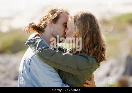 Ihre Liebe im Freien zum Ausdruck bringen. Ein liebevolles junges Paar, das sich einen Kuss in der Natur teilt. Stockfoto