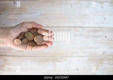 Hände, die einen Haufen Euro-Münzen in der Hand halten, auf Holzhintergrund. Spenden, Sparen, Spendenaktionen, Familienfinanzplan, Finanzkrisenkonzept. Draufsicht. Speicherplatz kopieren Stockfoto