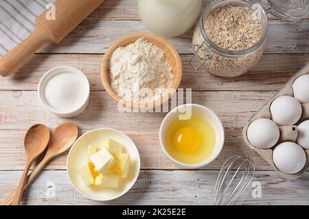 Rahmen aus Zutaten zum Backen auf weißem Hintergrund. Mehl, Eier, Zucker und Milch in weißen und hölzernen Schüsseln. Koch- und Backkonzept. Stockfoto