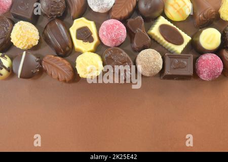 Schokoladenkekse und Pralinen für eine Ferienveranstaltung auf braunem Hintergrund mit großem Kopierplatz. Flach liegend