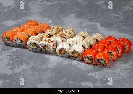 Verschiedene Arten von köstlichem und saftigem Sushi und Brötchen auf grauem Hintergrund Stockfoto