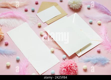 Leere Karten und ein Umschlag in der Nähe von Pastellblumen, Pompons und Federn in der Nähe des Rings in einer rosafarbenen Geschenkbox Stockfoto