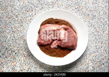 Ein Stück gewürztes Fleisch auf einem Teller vor dem Braten Stockfoto