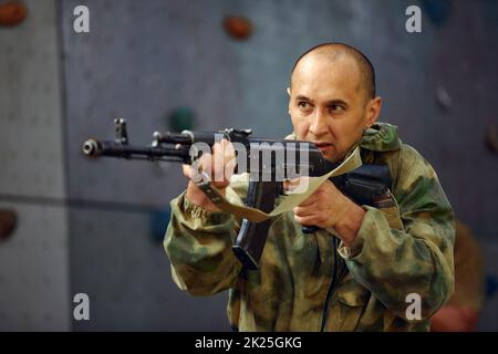 Der Soldat bei der Ausführung von Aufgaben in Tarnung und Schutzhandschuhen, hält eine Waffe. Die Zone der militärischen Operationen. Stockfoto