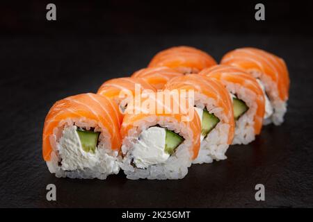 Sushi-Rolle mit Lachs, Avocado und Frischkäse auf schwarzem Hintergrund. Stockfoto