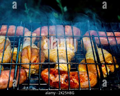 Hühnerschenkel und Fleischwürste auf einem eisernen Grillnetz über dem Feuer. Stockfoto