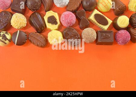 Pralinen mit Schokoladenkürbis zur Draufsicht. Schokoladenbonbons auf orangefarbenem Hintergrund. Schokoladenrahmen, Draufsicht. Schokoladenpralinen mit Kopierbereich für Text. Rand verschiedener Süßigkeiten Stockfoto