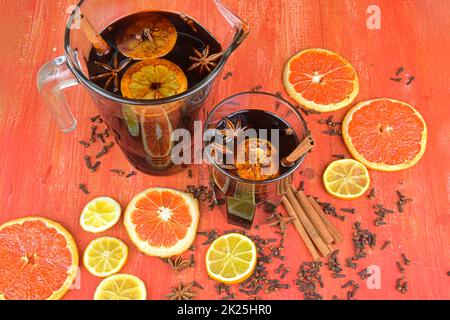 Heißer Glühwein mit Zimt, Nelken und Anisstern auf Holzhintergrund. Glühwein für Winter und Weihnachten auf einem rustikalen Holztisch. Roter heißer Wein in einem Krug Stockfoto