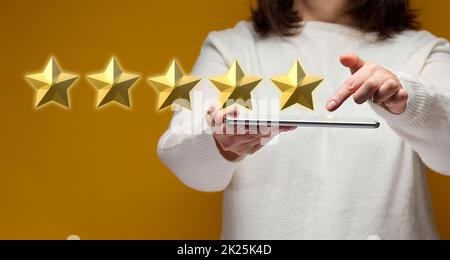 Weibliche Hand hält ein elektronisches Gadget-Tablet auf gelbem Hintergrund, fünf goldene Sterne Stockfoto