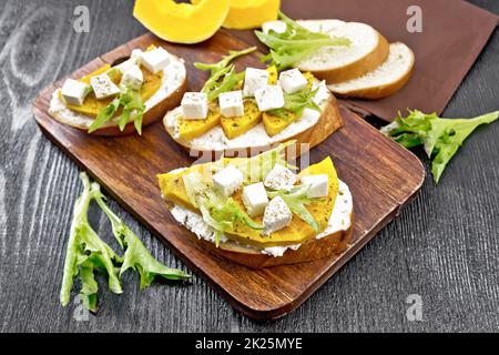 Bruschetta mit Kürbis und Rucola auf dunklem Brett Stockfoto