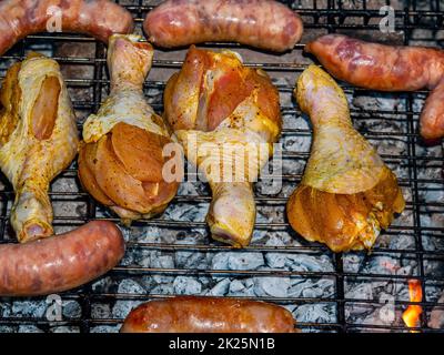 Hähnchenschenkel und Fleischwürste auf einem Eisengitter. Stockfoto