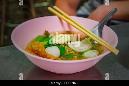Thailändische Nudelsuppe mit Fischbällchen, rosa Schüssel, Essstäbchen, Thailand. Stockfoto