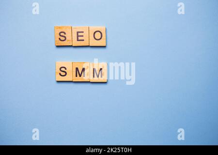 Die Holzbriefe SEO und SMM sind auf hellblauem Hintergrund gedruckt. Stockfoto