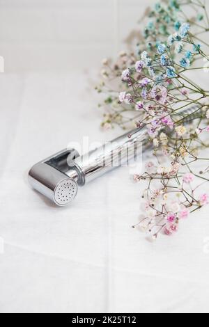 Hygiene- und Reinheitskonzept. Neue hygienisch verchromte Dusche in der Hand vor weißem Fliesenhintergrund. Badezimmer. Stockfoto