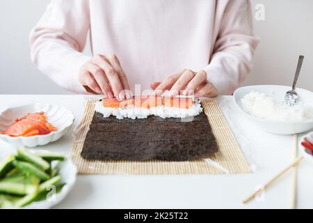 Sushi-Zubereitung, das Mädchen macht Sushi mit verschiedenen Geschmacksrichtungen - frischer Lachs, Kaviar, Avocado, Gurke, Ingwer, Reis. Stockfoto