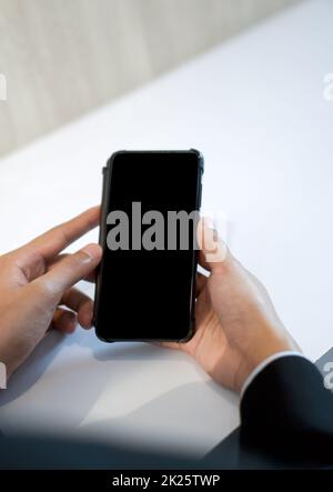 Geschäftsmann in schwarzem Anzug mit leerem Bildschirm Mobiltelefon mit beiden Händen. Stockfoto
