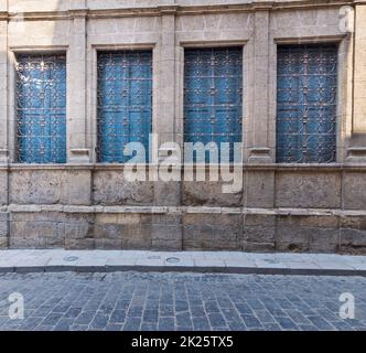 Fenster mit schmiedeeisernem Grill und blauen Fensterläden an alten Steinmauern und Basaltstraße Stockfoto