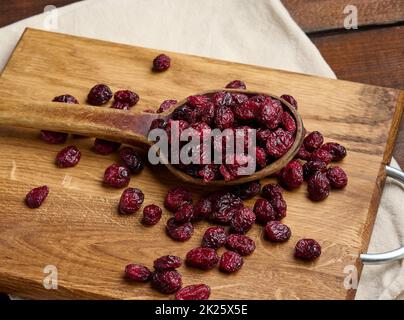 Ein paar getrocknete Preiselbeeren in einem Holzlöffel auf einem braunen Tisch. Köstliche Beeren, Blick von oben Stockfoto