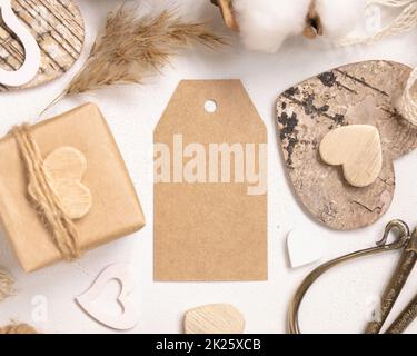 Leerer Geschenkanhänger zwischen Geschenk am Valentinstag, Draufsicht auf Herzen und getrocknete Blumen, russisches Label Mockup Stockfoto