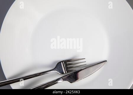 Leerer Teller mit Gabel und Messer auf grauem Hintergrund, Draufsicht für Kopierraum, Lebensmittel und gesundes Essenskonzept Stockfoto