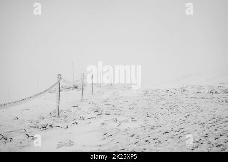 Kettenzäune bedeckt mit Eis und Schnee auf einem gefährlichen Abschnitt des Weges in den Bergen. Stockfoto