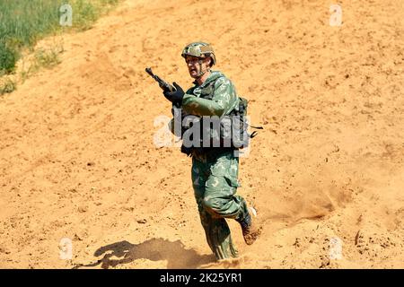 Der Soldat bei der Ausführung von Aufgaben in Tarnung und Schutzhandschuhen, hält eine Waffe. Die Zone der militärischen Operationen. Stockfoto