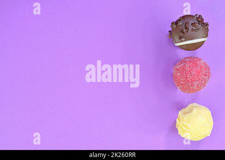 Sammlung von Schokoladenbonbons auf einem bunten Hintergrund. Schokoladenpralinen auf einem pastellfarbenen lila Hintergrund mit Kopierfläche. Flach liegend, Draufsicht Stockfoto