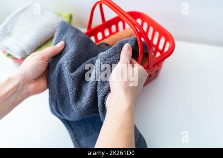 Bunte Handtücher liegen in einem roten Wäschekorb, eine Frau faltet ein Handtuch. Wäscherei und Bügeln. Stockfoto