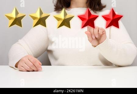 Customer Experience Feedback-Konzept. Fünf rote Sterne, die beste Bewertung für ausgezeichnete Dienstleistungen mit einer weiblichen Hand zu treffen. Weißer Tisch Stockfoto